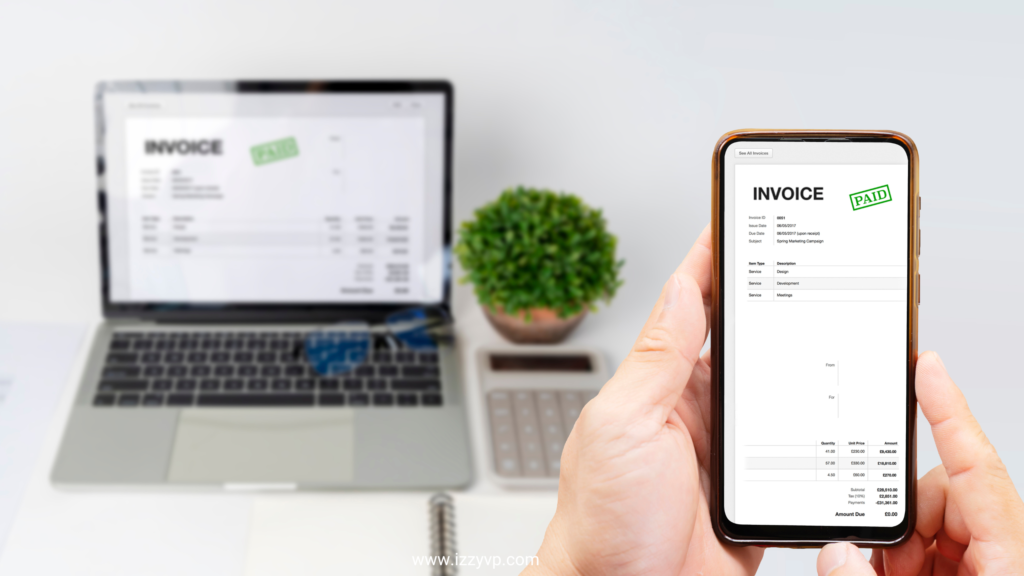 Hand holding a smartphone displaying a paid invoice, with the same invoice visible on a blurred laptop screen in the background.